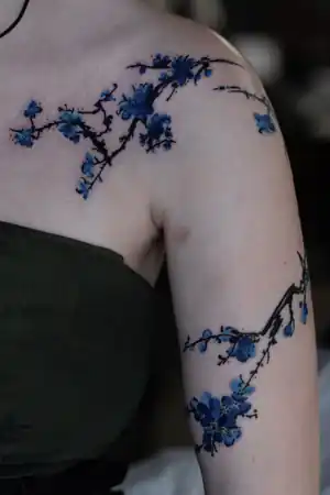 Blue blossom branch arm tattoo by Kristina Vishar